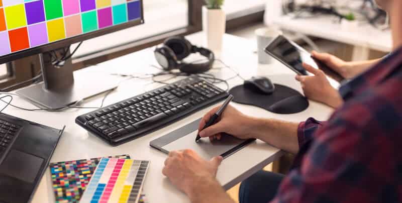 Webdesigner sitzt am braunen Schreibtisch mit einem Stift in der Hand