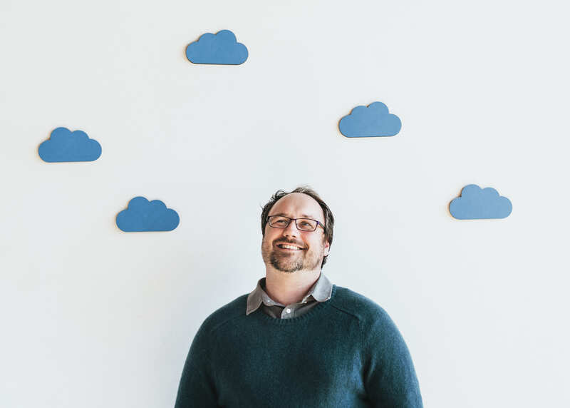 Lächelnder Mann steht vor einer Leinwand mit Kunstwolken